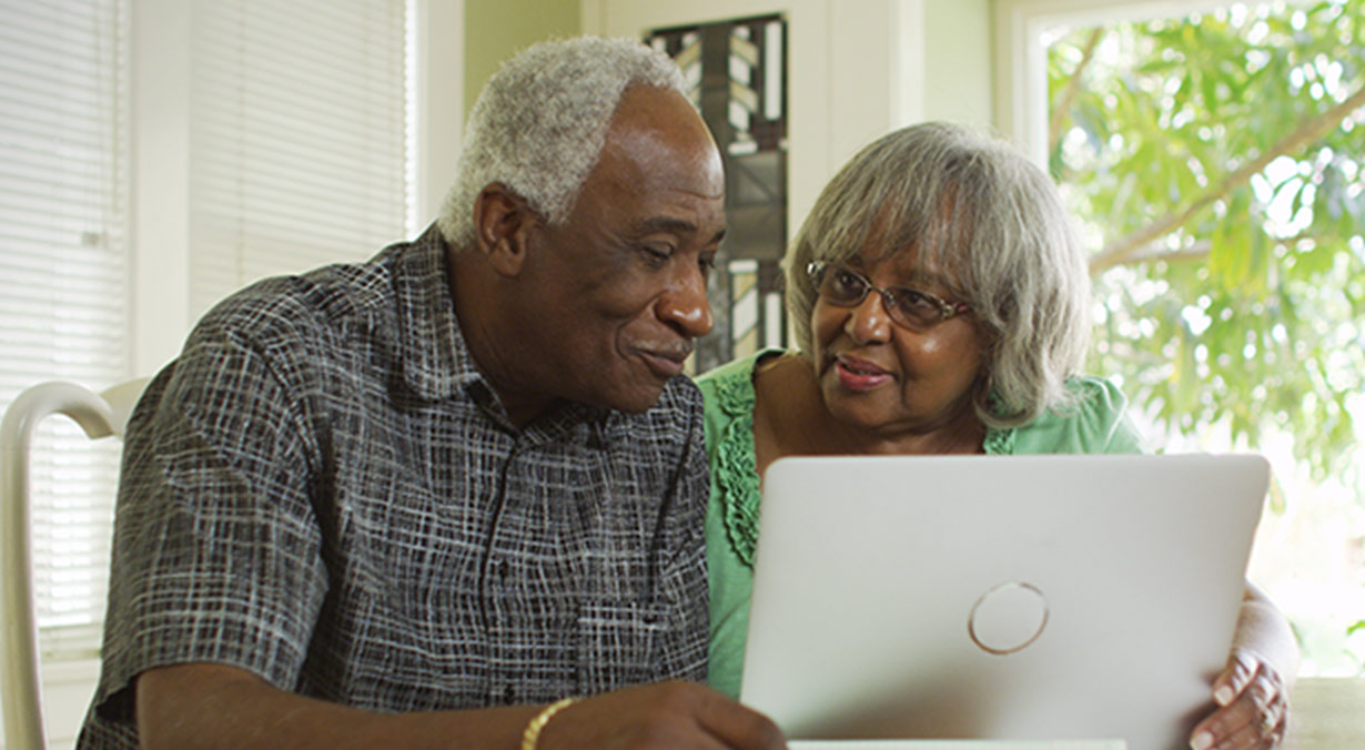 An African American man and woman smiling, looking at laptop at home