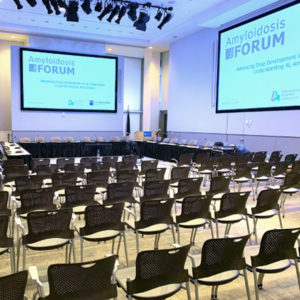 Conference room chairs in neat rows and TV screens showing Amyloidosis Forum presentation